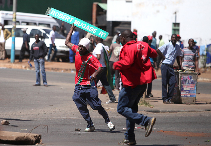   protester holds up a street sign with resident obert ugabes name on it as imbabwe opposition supporters clash with police during a protest march for electoral reforms on ugust 26 2016 in arare     