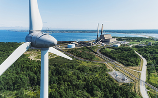 A wind turbine turns in the foreground of a coal fired power generating station | Credit: iStock