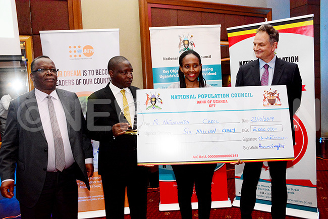  arol atukunda a senior writer with the ew ision receives a dummy cheque of sh6m from the state minister for finance avid ahati second left after she was declared overall winner of the opulation edia wards 2019 ight is the  country representative lain ibenaler and ational opulation ouncil board chairman r abwire angen