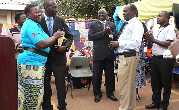 Omutandisi wa TASO Noerine Kaleeba ng'akwasa ekirabo abadde ssentebe wa TASO okumala emyaka mukaaga, Dr. Joseph Baguma ( ayambadde essuuti wakati) eyawumudde ku mukolo nga bajaguza okuweza emyaka 30 nga bajjanjaba abalwadde ba mukenenya n'okubabudaabuda. Omutandisi wa TASO Noerine Kaleeba ng'akwasa ekirabo abadde ssentebe wa TASO okumala emyaka mukaaga, Dr. Joseph Baguma ( ayambadde essuuti wakati) eyawumudde ku mukolo nga bajaguza okuweza emyaka 30 nga bajjanjaba abalwadde ba mukenenya n'okubabudaabuda.