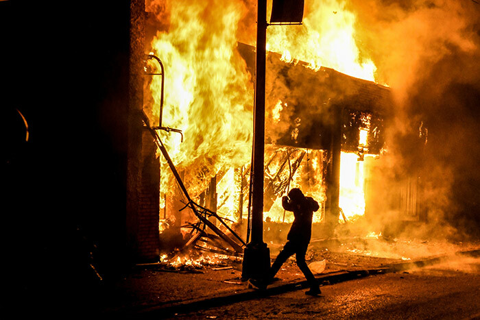 protester kicks a stone into a burning building set on fire during a demonstration in inneapolis innesota on ay 29 2020 over the death of eorge loyd a black man who died after a white policeman kneeled on his neck for several minutes hoto by handan