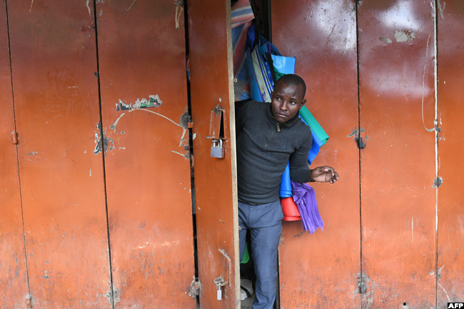   business man peeks out of his shop while closing his shop before the beginning of a curfew in enyas capital airobi