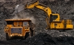 A huge excavator loads rock formation into the back of a heavy mining dump truck.