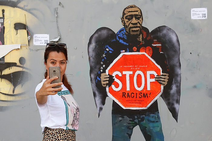 woman takes a selfie picture posing next to a street poster artwork by talian urban artist alvatore enintende aka depicting eorge loyd with angel wings and holding a stop traffic sign against racism in a street of arcelona on ay 31 2020 hoto by