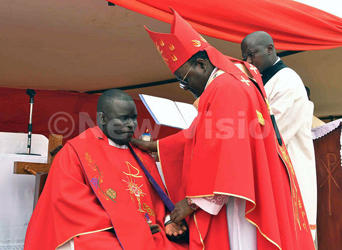  rchbishop of ampala r yprian izito wanga helps r oah serunjongis to sit in chair after announcing him officially as new arish riest of unnamwaya 