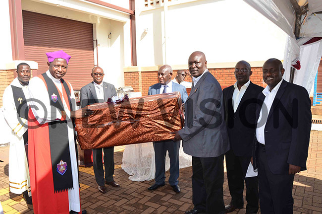 he utgoing rchbishop of the hurch of ganda tanley tagali secondleft receiving a digital weighing scale machine from r jom as other members of the oard of oint edical tore look on his was during tagalis farewell visit to the organisations headquarters in sambya on ednesday