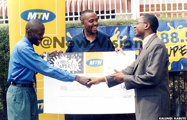  hillip esiimire m and eter ematimba hand over a cheque to a winner in a joint  and uper  promotion
