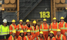 A group of women miners stand in front of large truck. 