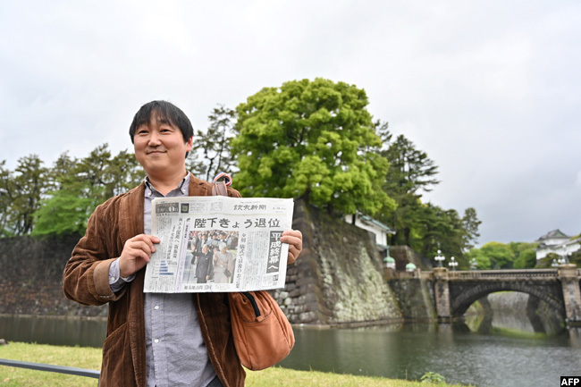   man holds a newspaper with an image of mperor kihito and mpress ichiko