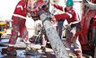 Workers in hard hats lift a drill