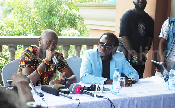 Kenzo (ku kkono) ng'ayogera mu lukungaana lw'abannamawulire. Kenzo (ku kkono) ng'ayogera mu lukungaana lw'abannamawulire.
