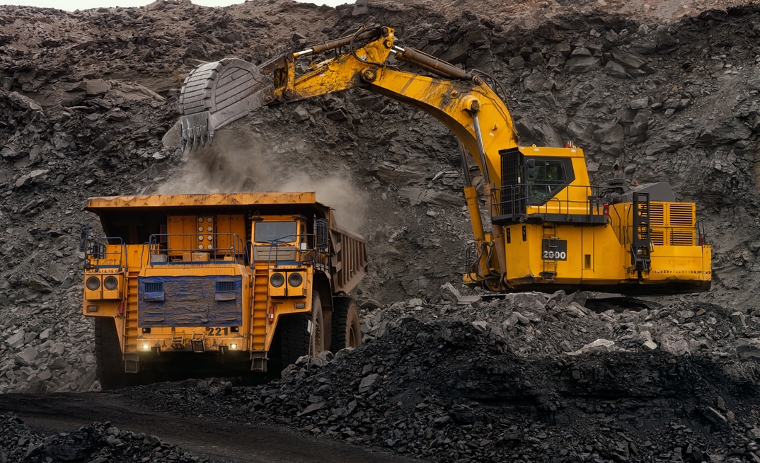 A huge excavator loads rock formation into the back of a heavy mining dump truck.