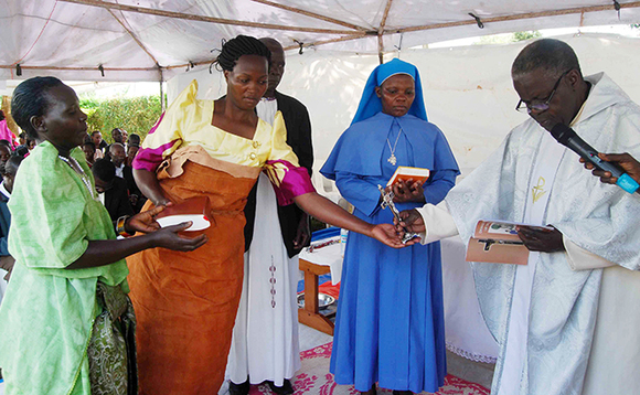 Msgr. Lawrence Kanyike (ku ddyo) ng'akwasa omusika wa Maria Nankusu Kawooya, Maria Nazziwa omusaalaba ogumulaga okwetikka emigugu gyonna okugikwasa Katonda mulumbe Msgr. Lawrence Kanyike (ku ddyo) ng'akwasa omusika wa Maria Nankusu Kawooya, Maria Nazziwa omusaalaba ogumulaga okwetikka emigugu gyonna okugikwasa Katonda mulumbe
